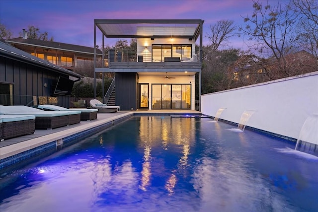 pool at dusk with a patio, pool water feature, outdoor lounge area, and ceiling fan