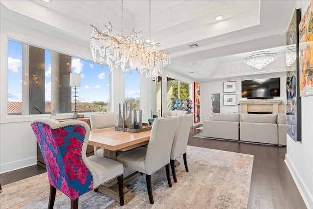 dining area with a healthy amount of sunlight, a chandelier, wood-type flooring, and a raised ceiling