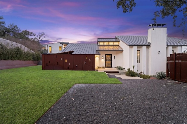 back house at dusk featuring a lawn