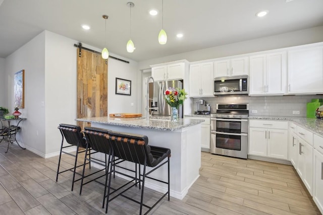 kitchen with a breakfast bar area, stainless steel appliances, an island with sink, and white cabinets