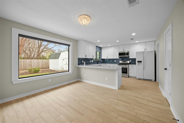 kitchen with sink, appliances with stainless steel finishes, tasteful backsplash, white cabinets, and kitchen peninsula