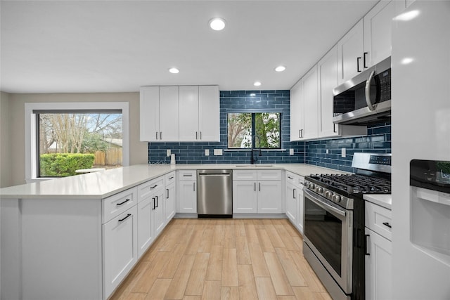 kitchen with white cabinetry, stainless steel appliances, kitchen peninsula, and sink