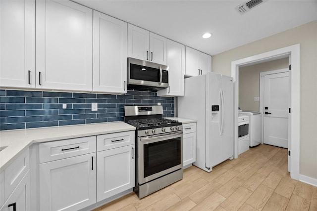 kitchen with stainless steel appliances, white cabinetry, backsplash, and light hardwood / wood-style flooring