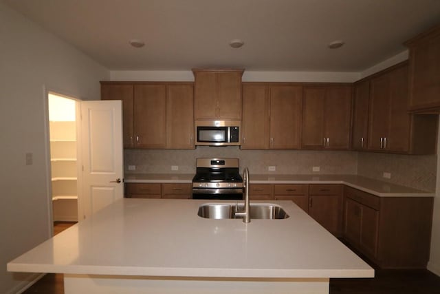 kitchen with stainless steel appliances, an island with sink, sink, and backsplash