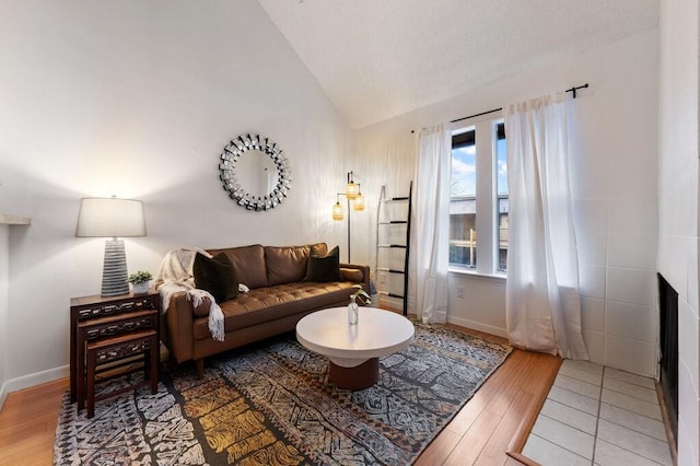 living room featuring a tile fireplace, vaulted ceiling, and wood-type flooring