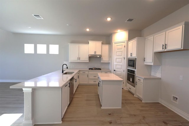 kitchen featuring a sink, light countertops, white cabinets, under cabinet range hood, and appliances with stainless steel finishes