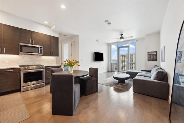 kitchen with dark brown cabinets, ceiling fan, stainless steel appliances, light hardwood / wood-style floors, and decorative backsplash