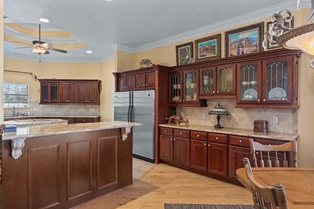 kitchen featuring stainless steel refrigerator, dark brown cabinetry, ornamental molding, and light stone countertops