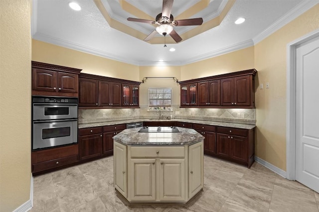 kitchen with double oven, decorative backsplash, dark stone counters, a center island, and a tray ceiling