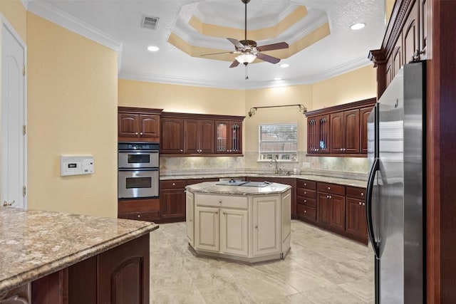 kitchen featuring crown molding, appliances with stainless steel finishes, backsplash, a center island, and a tray ceiling