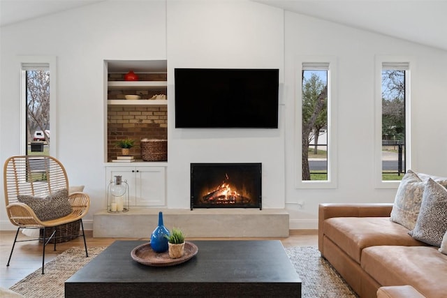 living area featuring a high end fireplace, plenty of natural light, wood finished floors, and vaulted ceiling