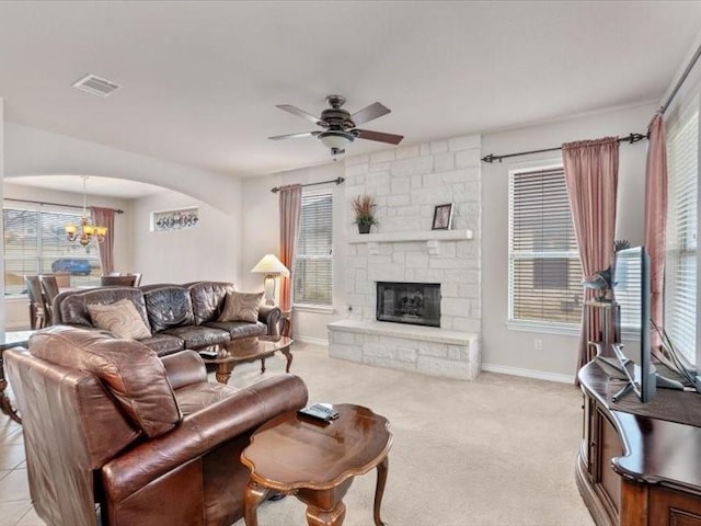 carpeted living room with a stone fireplace and ceiling fan with notable chandelier