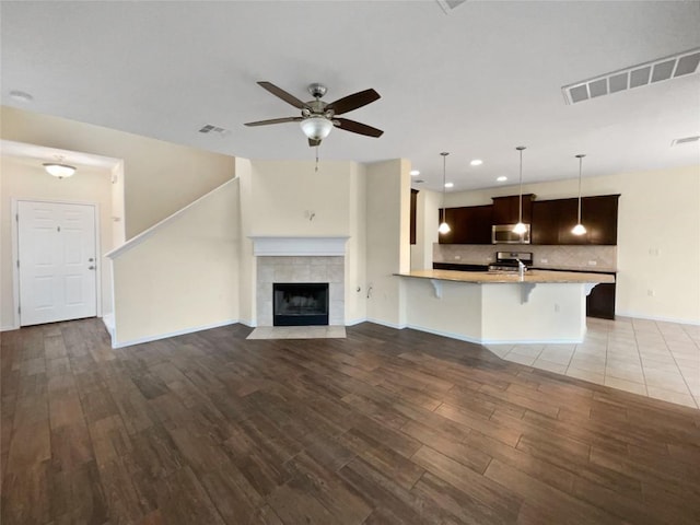 unfurnished living room with ceiling fan, dark hardwood / wood-style flooring, and a tiled fireplace