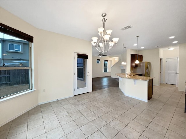 kitchen featuring light tile patterned flooring, a breakfast bar area, decorative light fixtures, stainless steel refrigerator, and kitchen peninsula