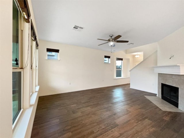 unfurnished living room with a tiled fireplace, ceiling fan, and dark hardwood / wood-style flooring