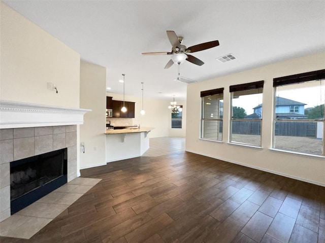 unfurnished living room featuring ceiling fan with notable chandelier, dark wood-type flooring, and a tile fireplace