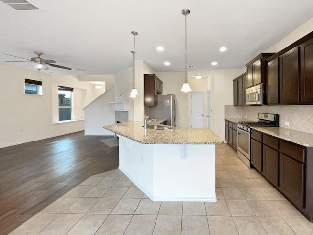 kitchen featuring pendant lighting, appliances with stainless steel finishes, a kitchen breakfast bar, light stone counters, and decorative backsplash