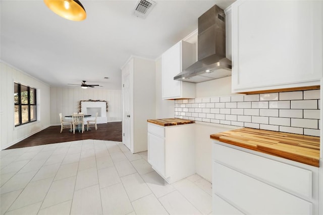 kitchen with white cabinetry, wall chimney exhaust hood, wooden counters, and tasteful backsplash