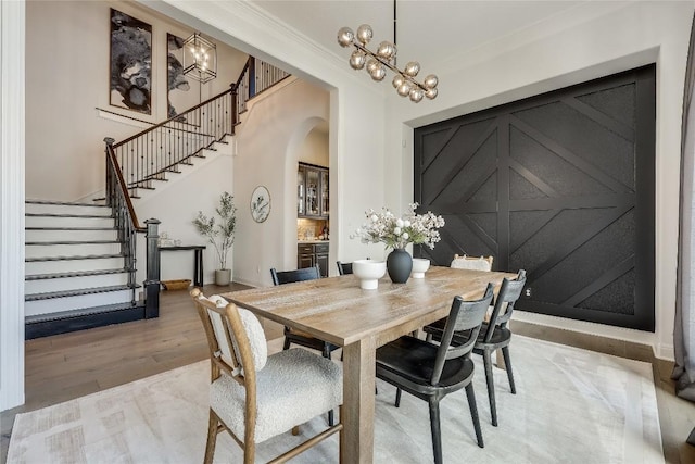 dining space featuring arched walkways, a notable chandelier, light wood-style floors, stairs, and crown molding