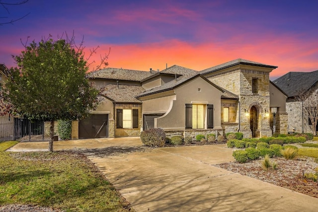 french country inspired facade with stucco siding, an attached garage, fence, stone siding, and driveway