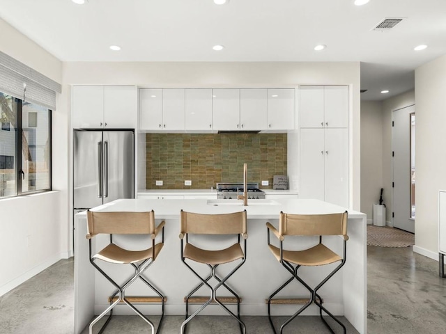 kitchen featuring a breakfast bar, sink, an island with sink, white cabinets, and backsplash