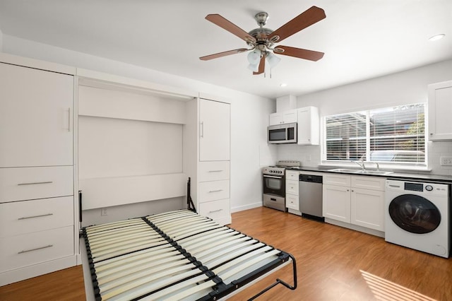 kitchen with appliances with stainless steel finishes, washer / clothes dryer, white cabinetry, sink, and light wood-type flooring