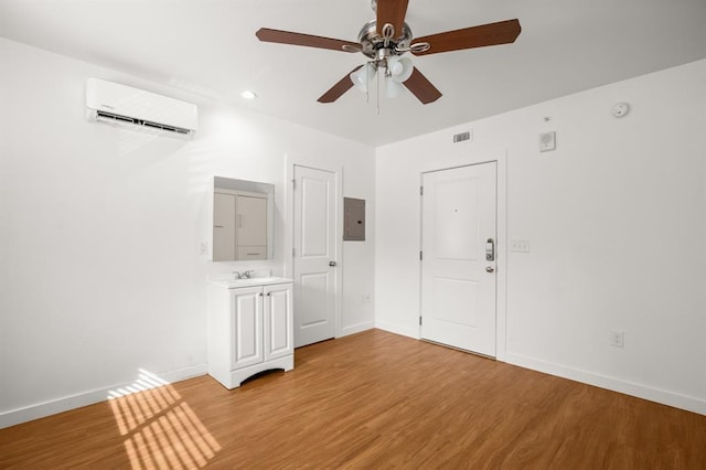 spare room featuring sink, light hardwood / wood-style flooring, an AC wall unit, electric panel, and ceiling fan