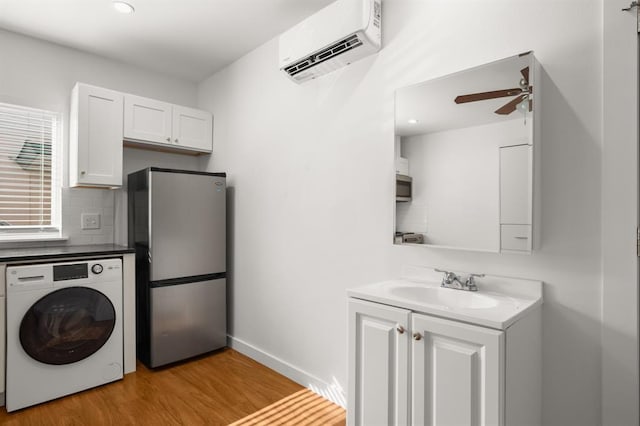 laundry area with sink, light hardwood / wood-style flooring, ceiling fan, a wall mounted AC, and washer / dryer