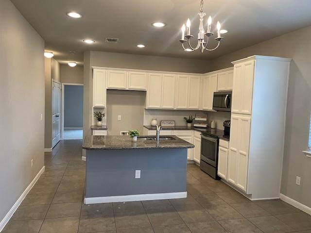 kitchen featuring sink, appliances with stainless steel finishes, dark stone countertops, white cabinets, and a center island with sink