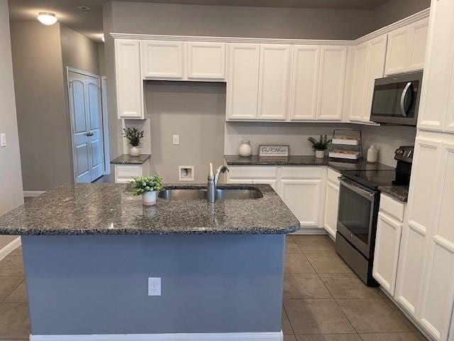 kitchen with electric stove, sink, white cabinets, a center island with sink, and dark stone counters