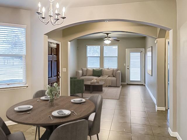 dining area with ceiling fan with notable chandelier, arched walkways, baseboards, and light tile patterned floors