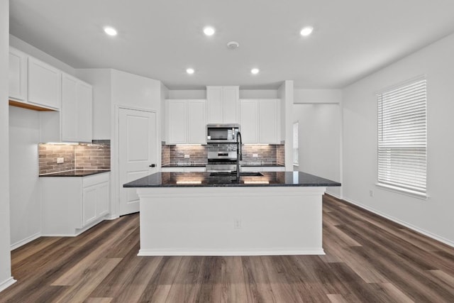 kitchen featuring dark wood-style floors, appliances with stainless steel finishes, tasteful backsplash, and a kitchen island with sink