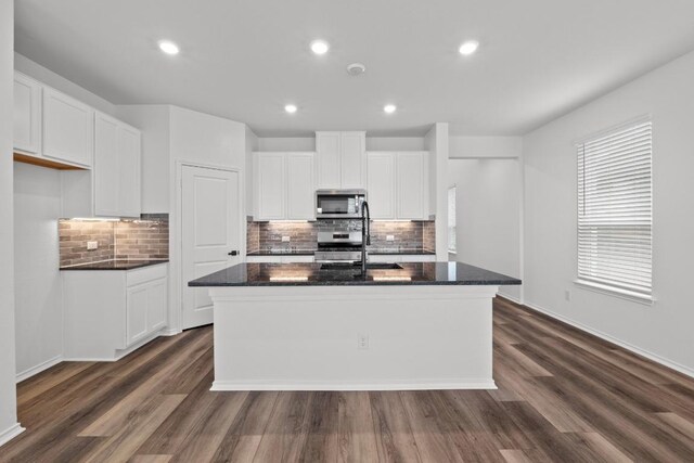 4829 Mozzafiato Ln, Round Rock, TX 78665 - kitchen featuring stainless steel microwave, a kitchen island with sink, tasteful backsplash, dark wood-style floors, and recessed lighting