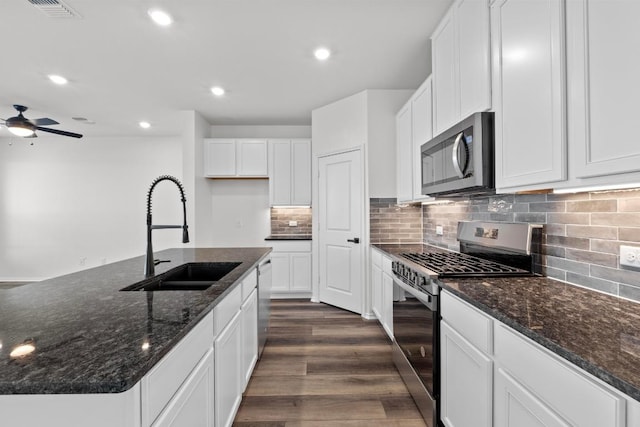 kitchen with recessed lighting, a sink, dark wood-type flooring, dark stone counters, and appliances with stainless steel finishes