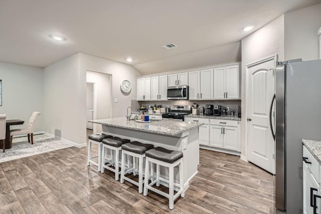 kitchen featuring appliances with stainless steel finishes, a breakfast bar area, white cabinets, light stone counters, and a center island with sink