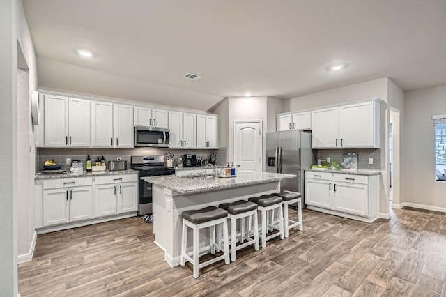 kitchen with a breakfast bar, white cabinetry, appliances with stainless steel finishes, an island with sink, and light stone countertops