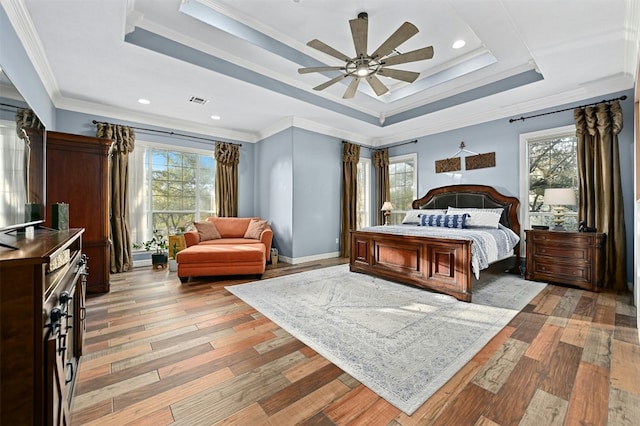 bedroom with crown molding, a tray ceiling, multiple windows, and light wood-type flooring