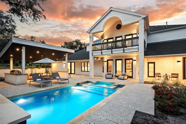 back of property at dusk featuring an outdoor kitchen, a balcony, brick siding, outdoor dry bar, and a patio area