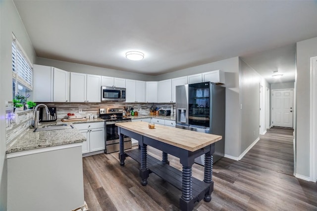 kitchen with appliances with stainless steel finishes, sink, white cabinets, light stone counters, and dark wood-type flooring