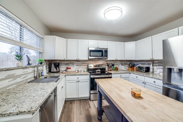 kitchen with sink, stainless steel appliances, light stone counters, tasteful backsplash, and white cabinets