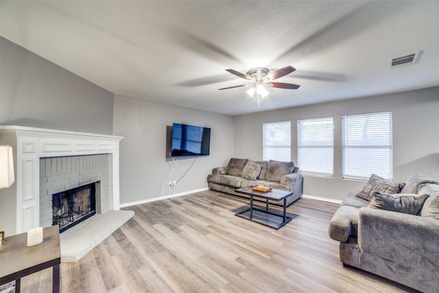 living room featuring a brick fireplace, a textured ceiling, light hardwood / wood-style floors, and ceiling fan