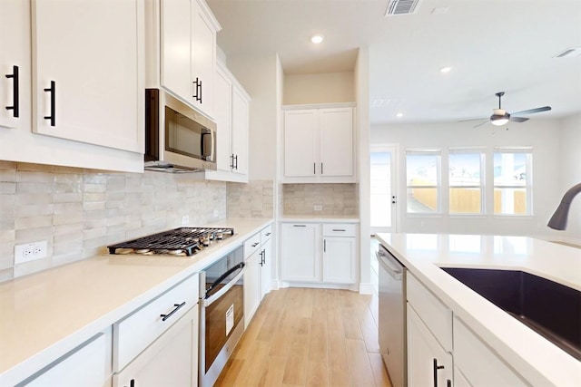 kitchen featuring tasteful backsplash, appliances with stainless steel finishes, light countertops, white cabinetry, and a sink