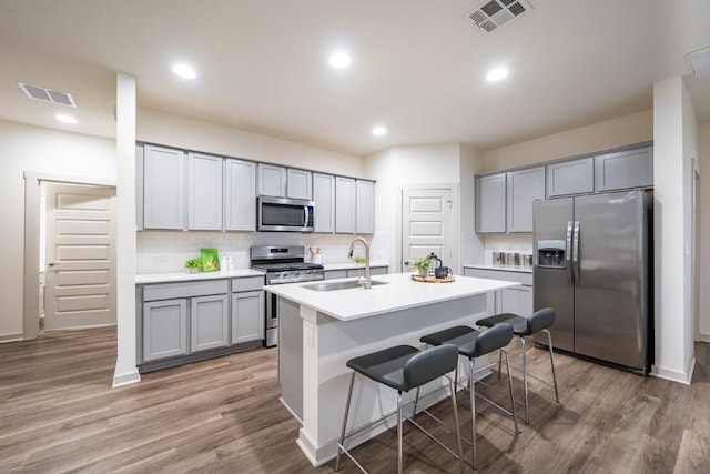 kitchen with sink, hardwood / wood-style flooring, a kitchen island with sink, stainless steel appliances, and a kitchen breakfast bar