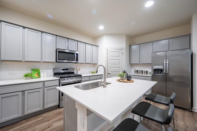 kitchen with stainless steel appliances, a kitchen island with sink, sink, and gray cabinetry