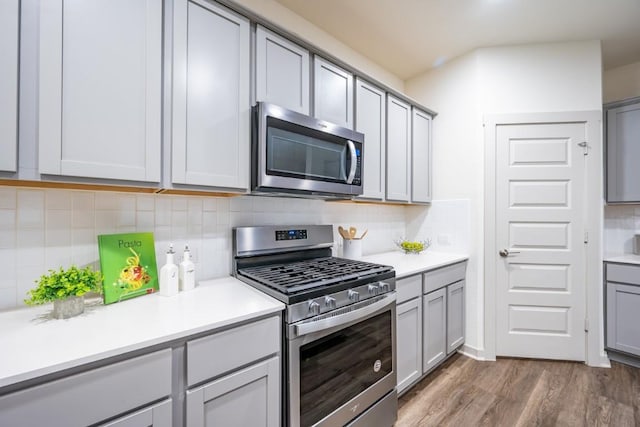 kitchen with gray cabinetry, dark hardwood / wood-style flooring, tasteful backsplash, and appliances with stainless steel finishes