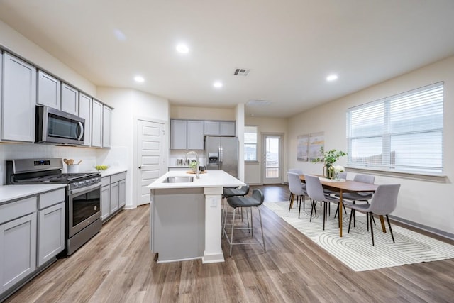 kitchen with gray cabinetry, sink, an island with sink, and appliances with stainless steel finishes