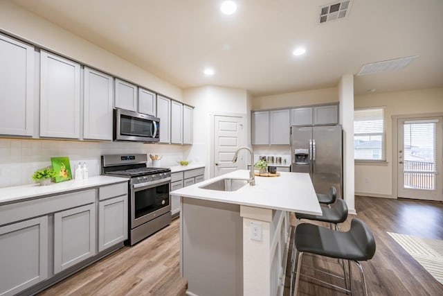 kitchen featuring a breakfast bar, sink, appliances with stainless steel finishes, gray cabinets, and a kitchen island with sink