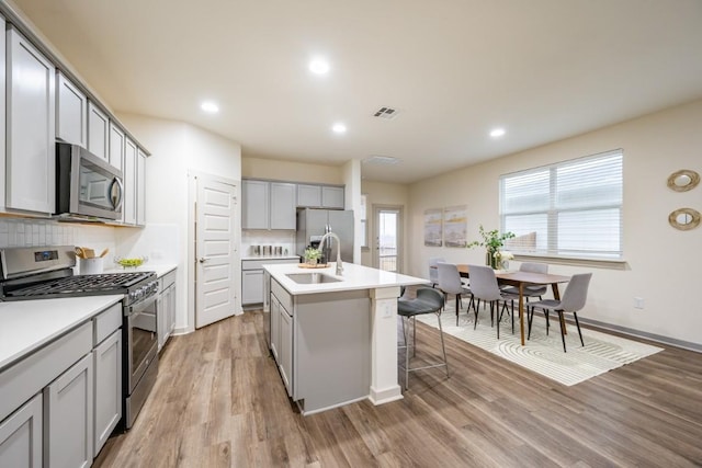 kitchen with sink, gray cabinetry, appliances with stainless steel finishes, an island with sink, and light hardwood / wood-style floors