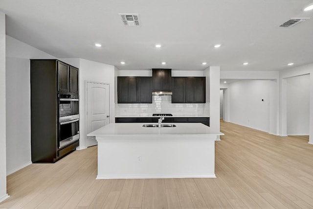 kitchen featuring an island with sink, visible vents, tasteful backsplash, and a sink