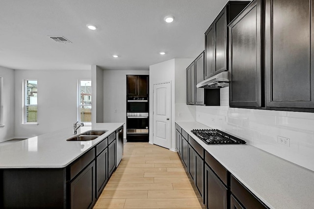 kitchen with under cabinet range hood, a sink, visible vents, light wood-style flooring, and appliances with stainless steel finishes